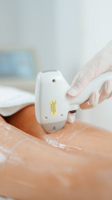 A close-up image showing a healthcare professional wearing white gloves using a handheld device to perform a medical procedure on a person's lower back, which is partially exposed and covered with transparent plastic wrap. The background is blurred, indicating an indoor clinical setting. This image illustrates the type of equipment and techniques used during medical or therapeutic treatments, which may be relevant in the context of home health support during a house move or in medical-related moving services offered by companies like Man with Van Hornchurch.